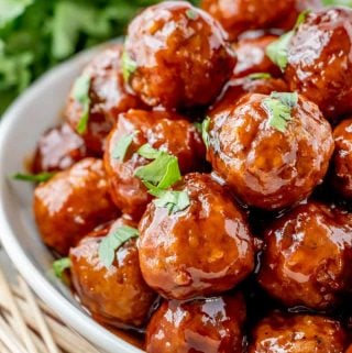 Meatballs stacked on top of one another on white serving tray topped with chopped parsley