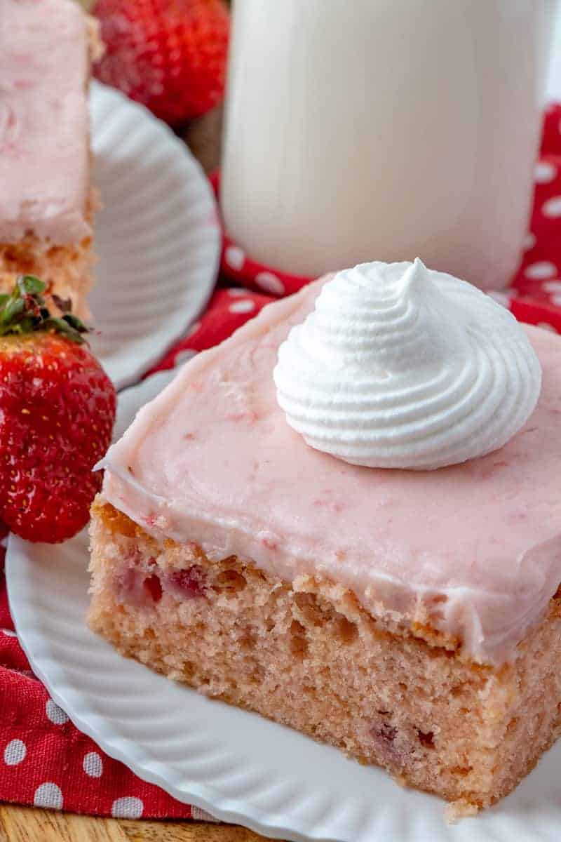 Slice of strawberry cake on plate with whipped cream, milk in background