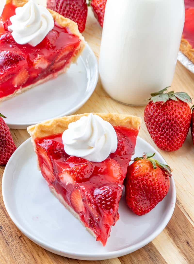 Strawberry pie on white plate with whole strawberries and milk in background