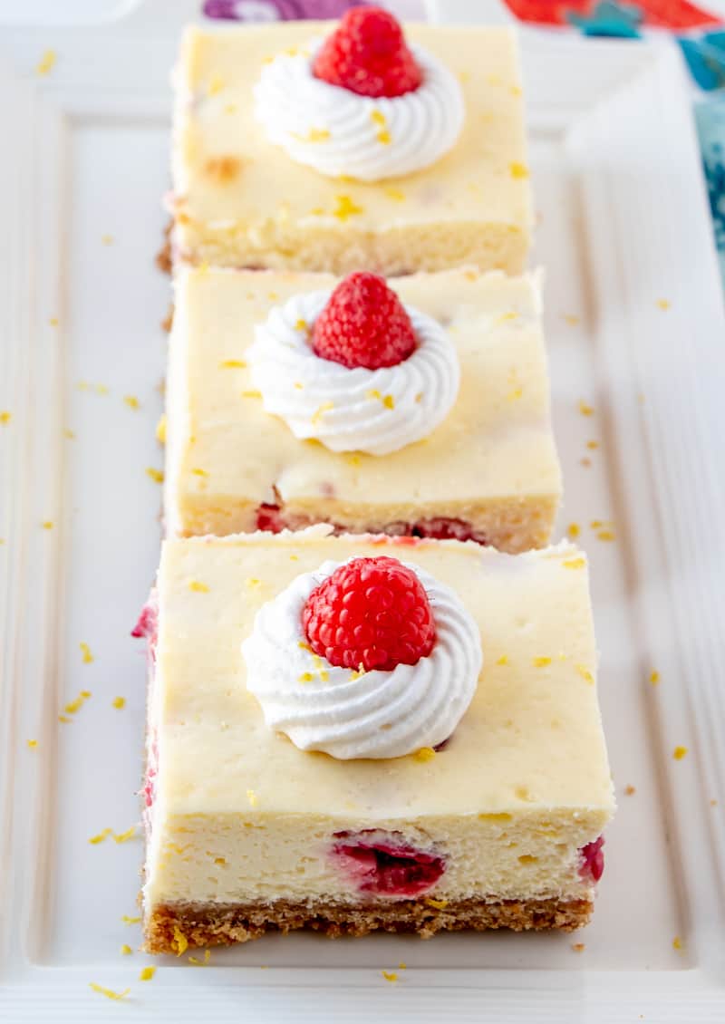 Lemon Raspberry Cheesecake Bars lined on white plate