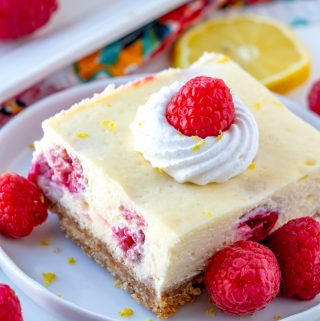 Lemon Raspberry Cheesecake Bars on plate topped with whipped cream and raspberry