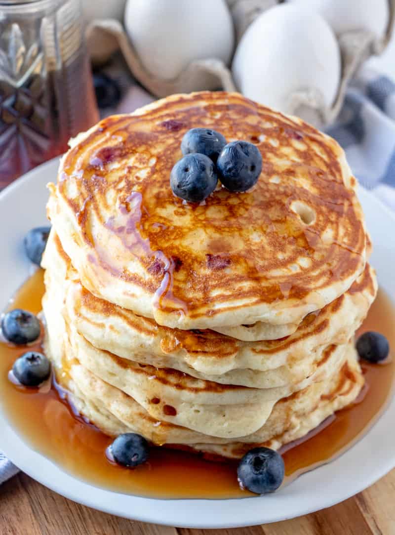 Blueberry Pancakes on plate with syrup dipping down and blueberries on top