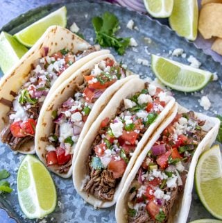 Overhead of four street tacos surrounded by lime wedges and cilantro