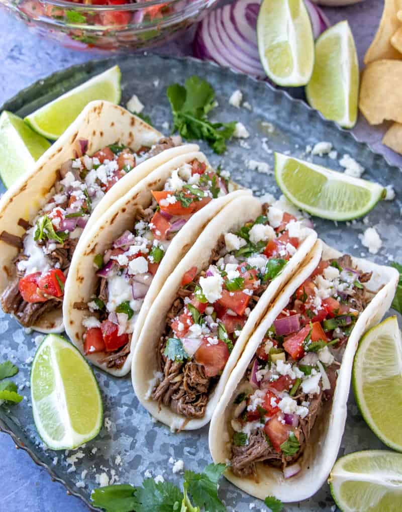 Overhead photo of 4 street tacos serving tray with limes