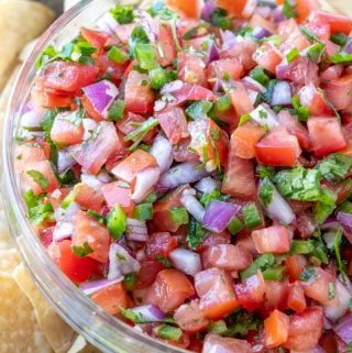 Close up of Pico de Gallo in clear bowl surrounded by tortilla chips