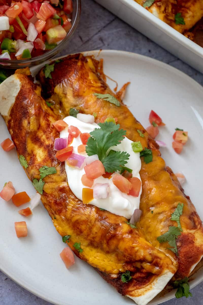 Sour cream and pico de Gallo topped over 2 enchiladas on plate with melted cheese