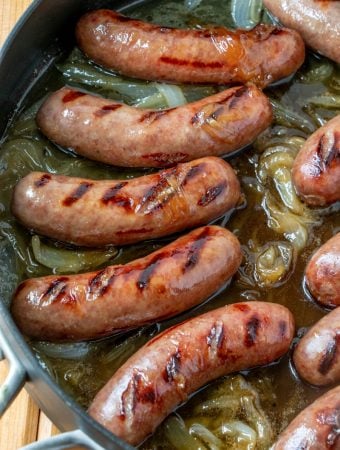 Overhead of grilled brats in saute pan with reduced beer and tender onions