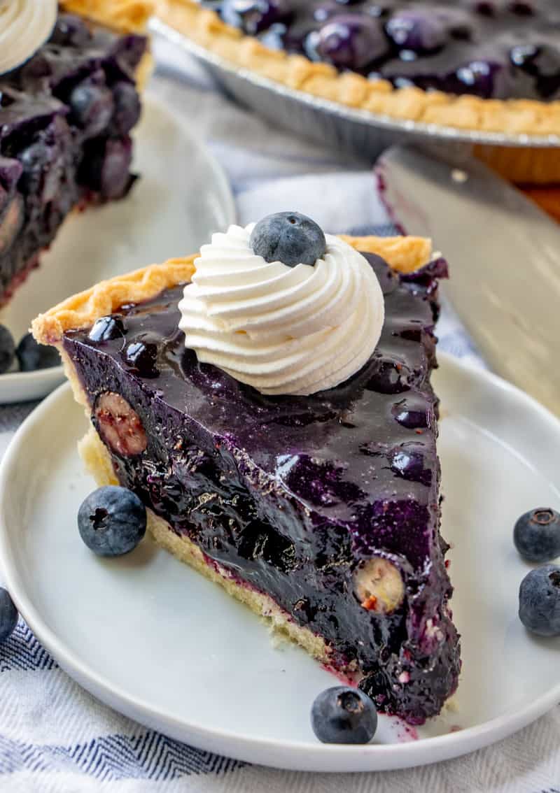blueberry pie on plate with whipped topping and blueberry on top