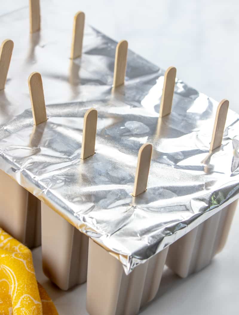 cover and tin foil placed on popsicle molds with popsicle sticks inserted