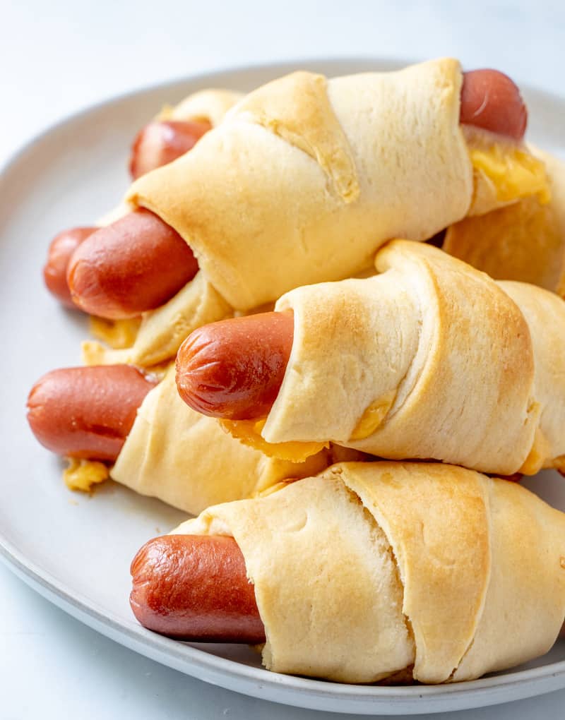 Hot dogs wrapped in cheese and crescent rolls layered on plate