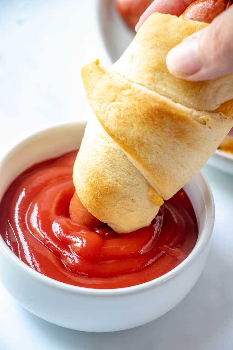hand dunking crescent dog in ketchup