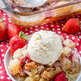 Cobbler on plate topped with ice cream and garnished with whole strawberries