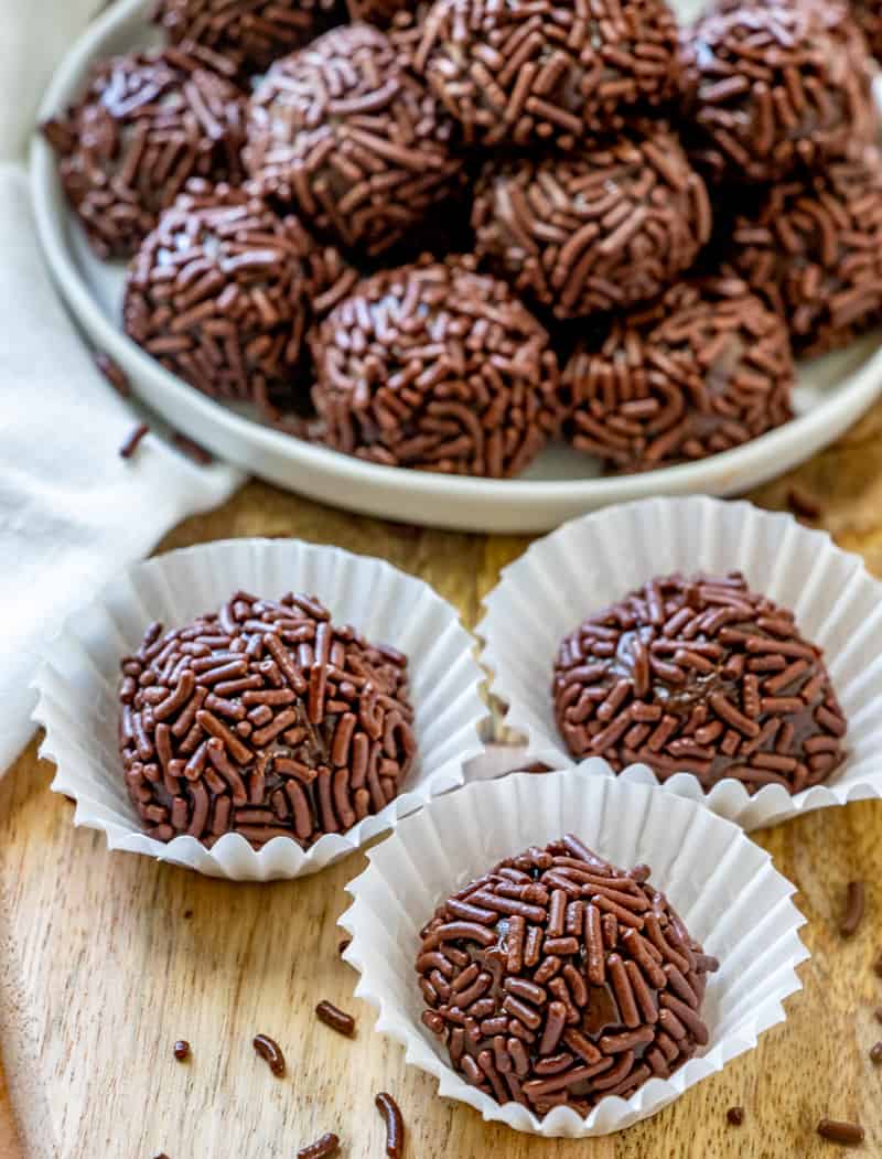 Brigadeiro recipe in mini cupcake liners with more stacked on plate behind