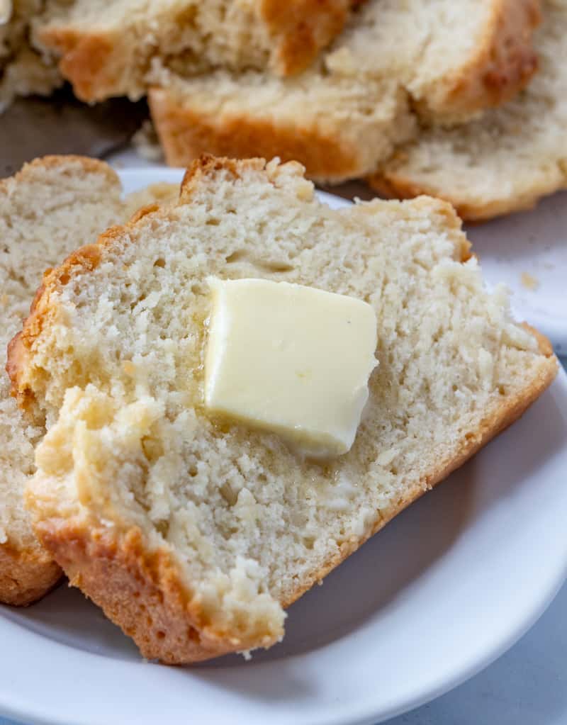 Up close photo of slice of beer bread on white plate with pat of butter melting