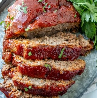 Sliced meatloaf garnished with parsley on metal serving tray