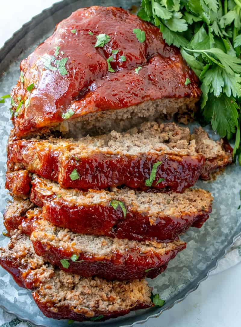 Slow cooker meatloaf on tray, sliced with tangy glaze, sprinkled in parsley