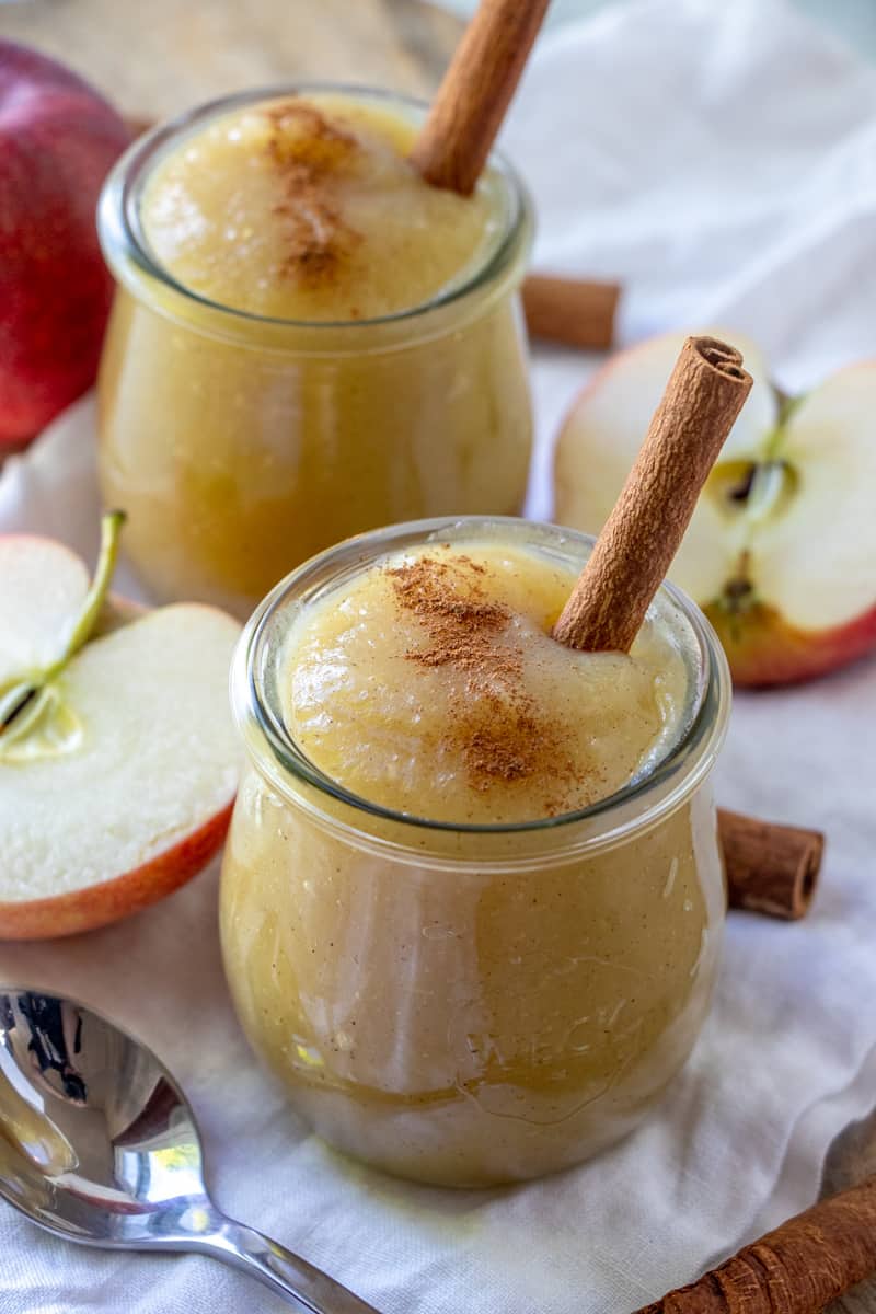 Applesauce in small jars with cinnamon sticks and a sprinkle of cinnamon on top of each