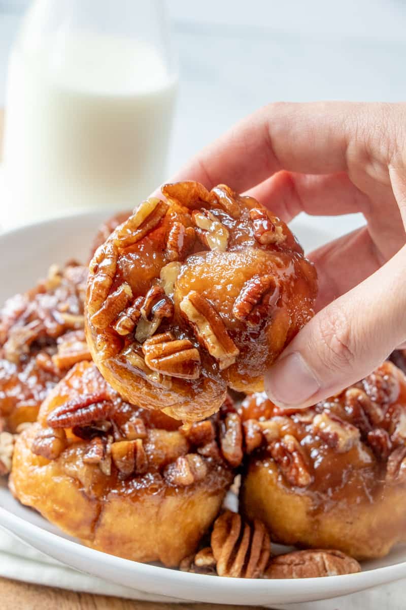 Hand holding sticky bun with milk and stacked buns in background