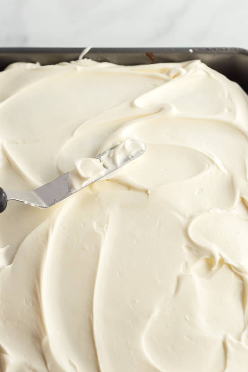 Cream cheese frosting being smoothed onto spice cake