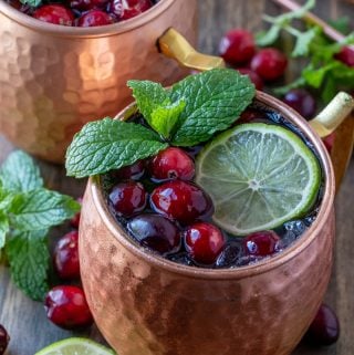 Two mugs filled with Moscow mules with cranberries, lime and mint