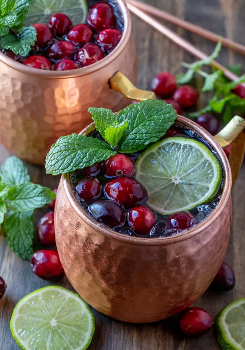 Cranberry Moscow Mules in two copper mugs with cranberries mint and limes