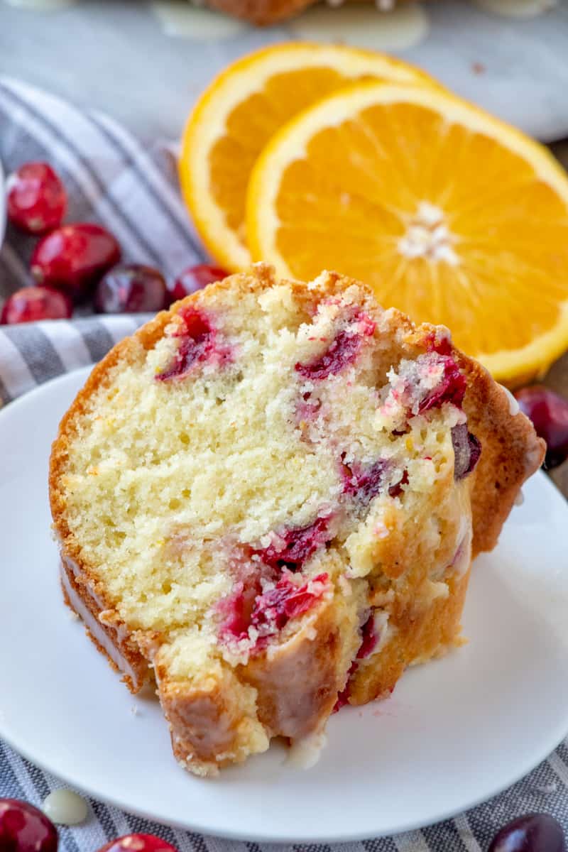Slice of Cranberry Orange Bundt Cake on plate with oranges and cranberries