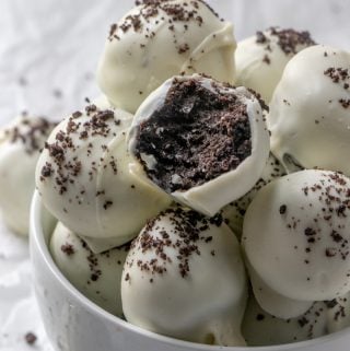 Oreo truffles stacked on top of one another in white bowl, bite taken out of one truffle