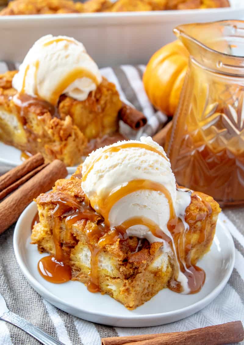 Two slices of bread pudding with ice cream and caramel sauce with cinnamon sticks and jar of caramel topping