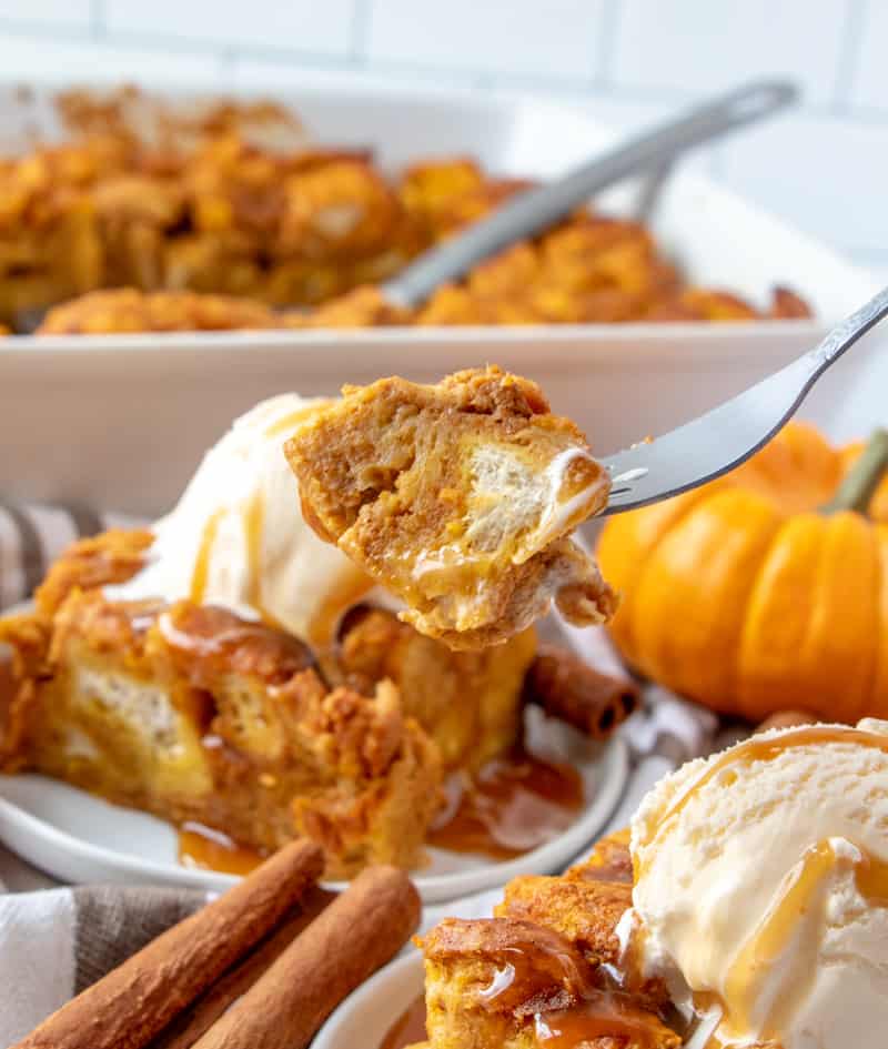 Bite of pumpkin bread pudding on fork with casserole dish in background