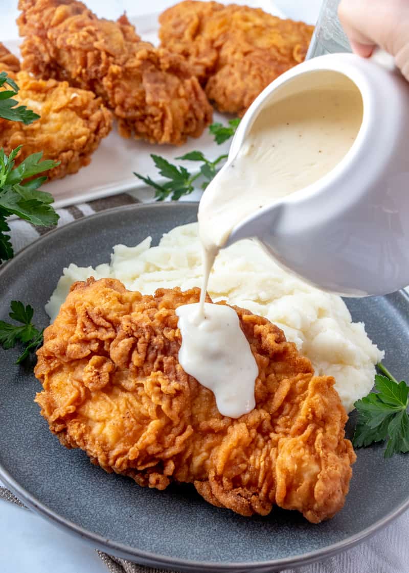 Gravy being poured over a piece of chicken fried chicken and mashed potatoes