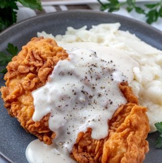 Pepper gravy drizzled over fried chicken piece on mashed potatoes