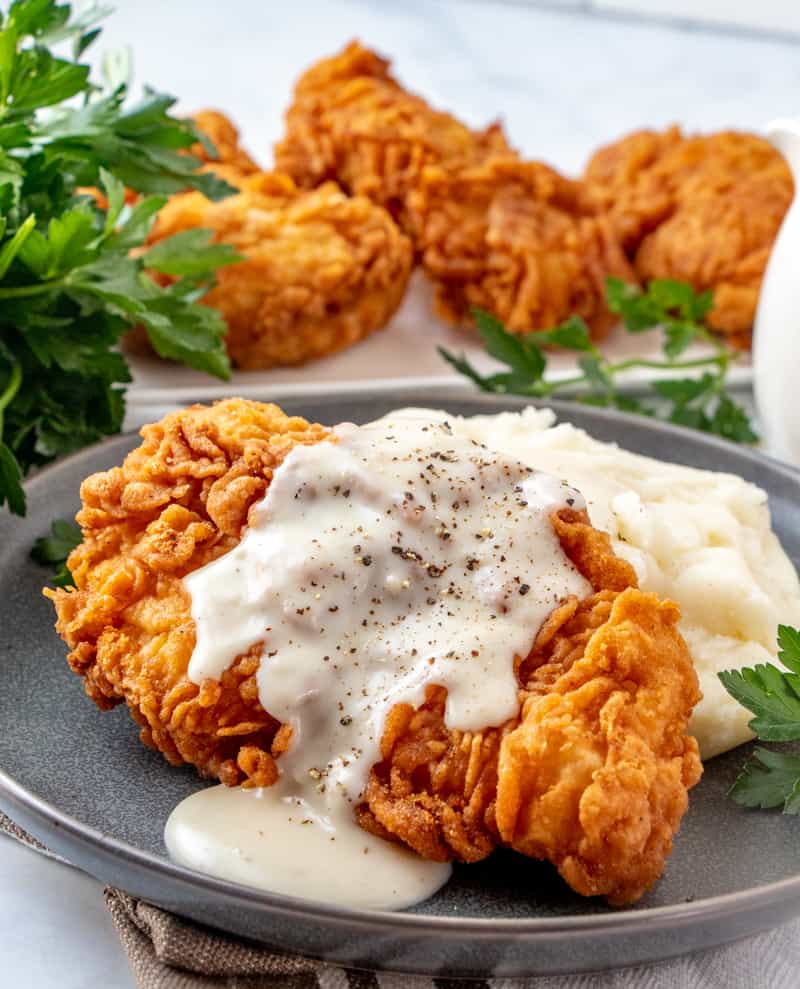 Chicken fried chicken piece on plate over mashed potatoes with fried chicken in background