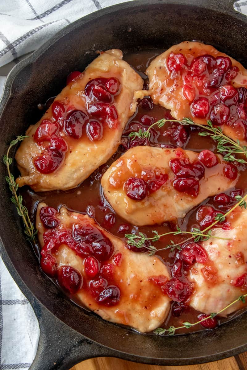 Overhead photo of cranberry chicken recipe in skillet with cranberry sauce over chicken pieces and thyme garnish