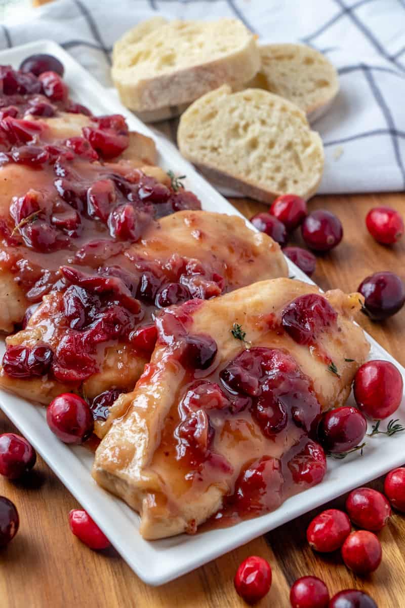 Cranberry Chicken on white serving plate with sliced bread in background