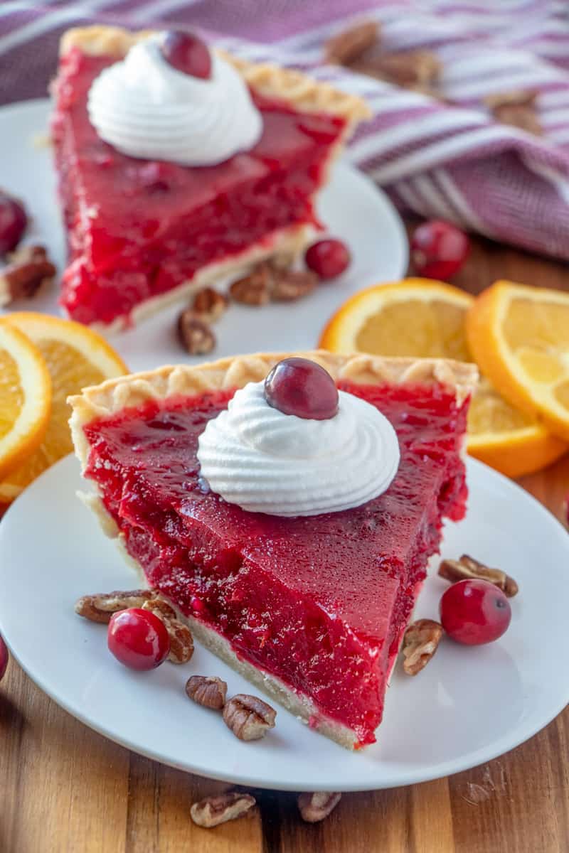Two slices of cranberry pie on plates slices of oranges surrounding as garnish