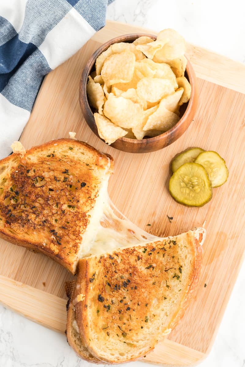 Overhead photo of grilled cheese cut in half showing melted cheese with chips and pickles