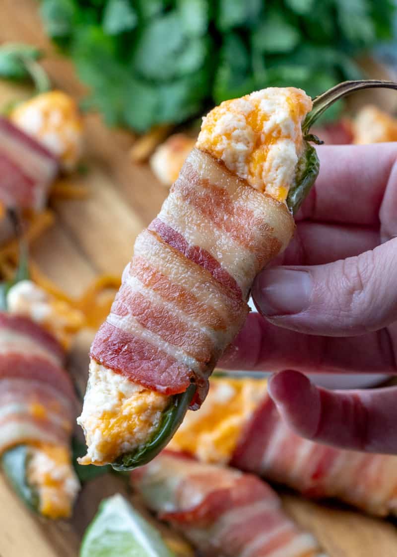 Hand holding jalapeno popper showing gooey cheese and crispy bacon