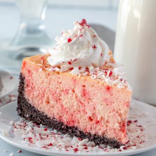peppermint cheesecake on white plate topped with whipped topping and crushed candy canes
