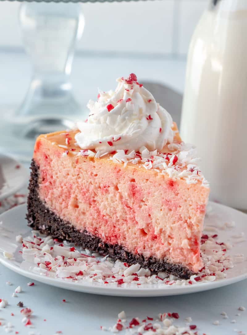 Slice of Peppermint Cheesecake on white plate with crushed candy canes and topped with whipped topping