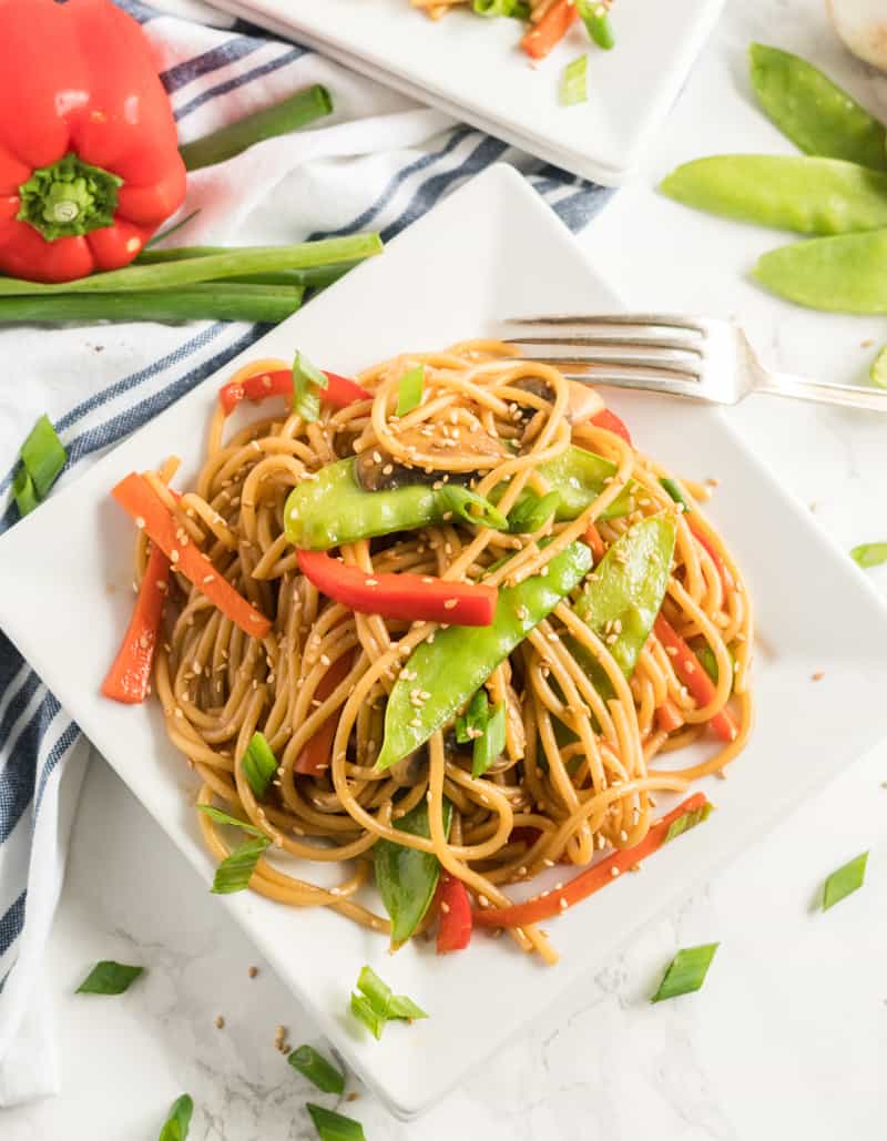 Plated Vegetable Lo Mein on square white plate surrounded by red pepper, green onions and pea pods