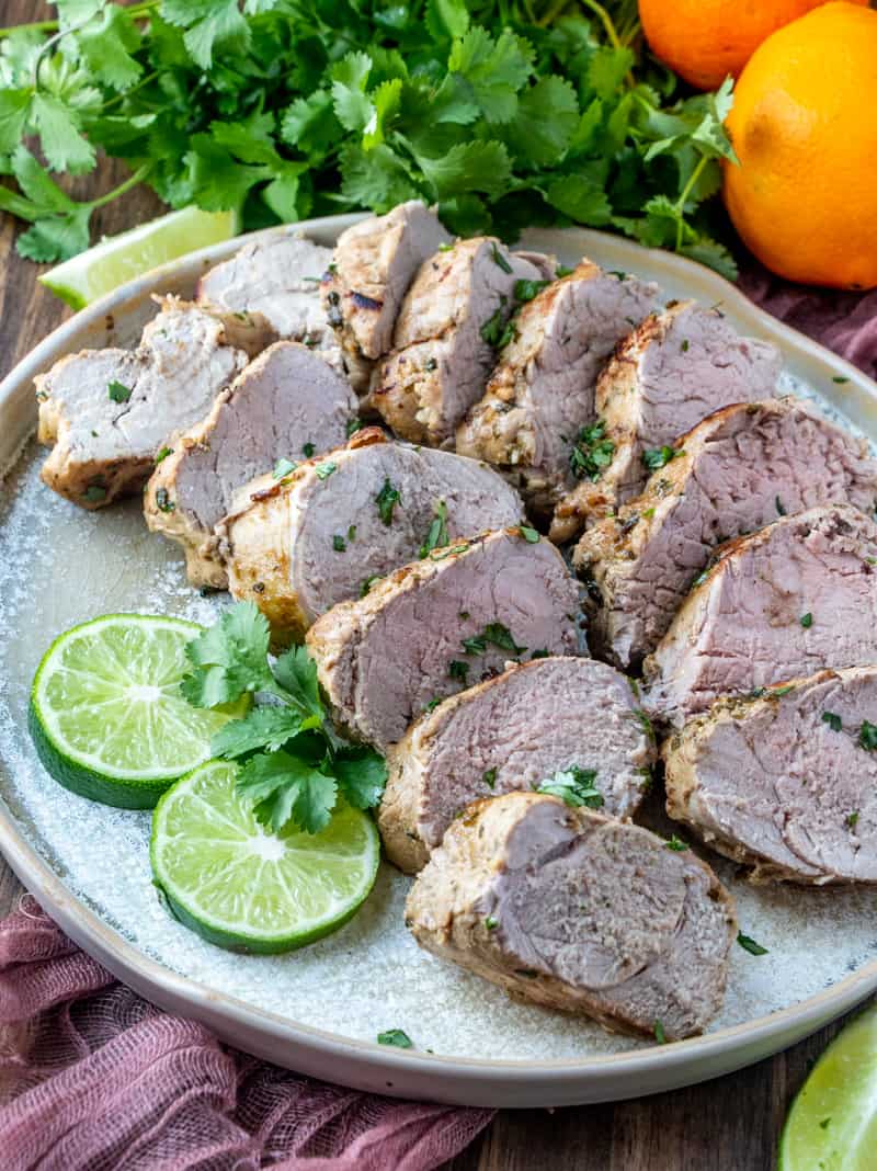 Sliced pork on plate with lime slices and oranges and cilantro in the back