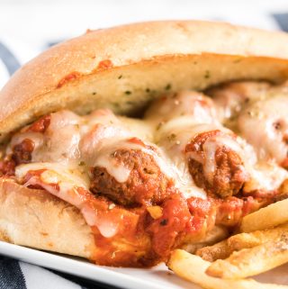 Closed meatball sub on white plate showing sauce, meatballs and melted cheese