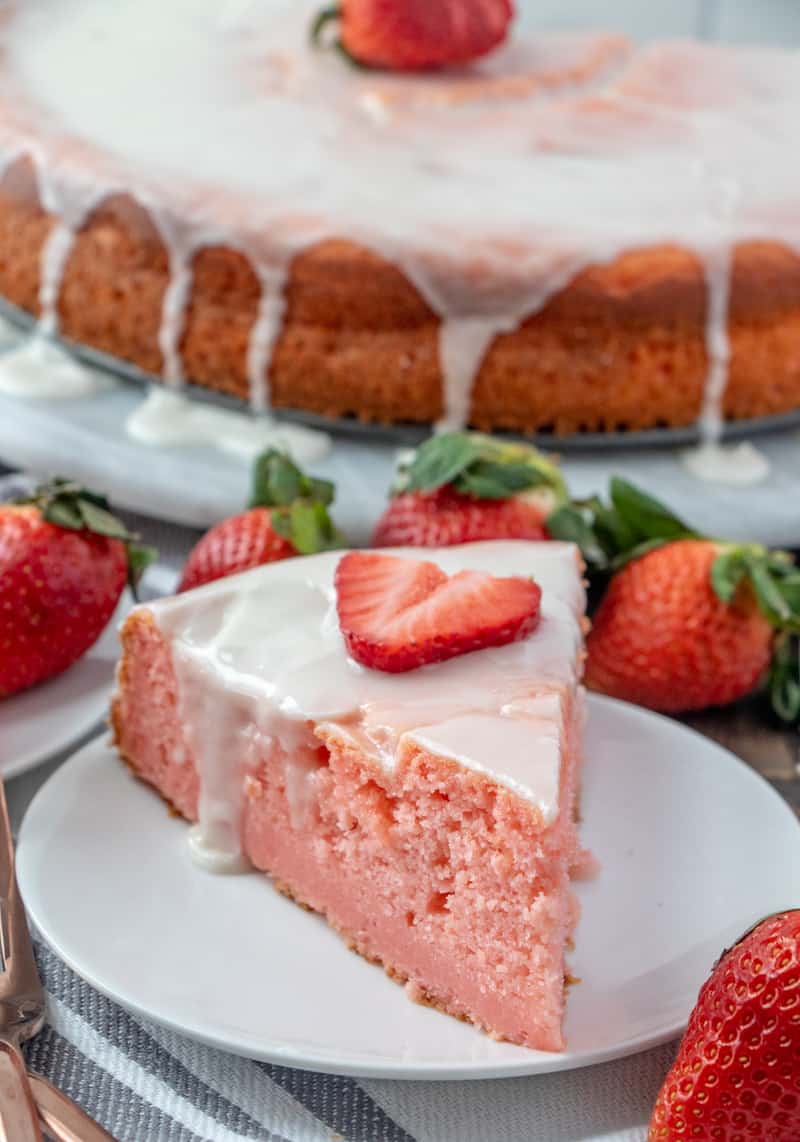 Slice of ricotta cake on white plate with sliced strawberry one top