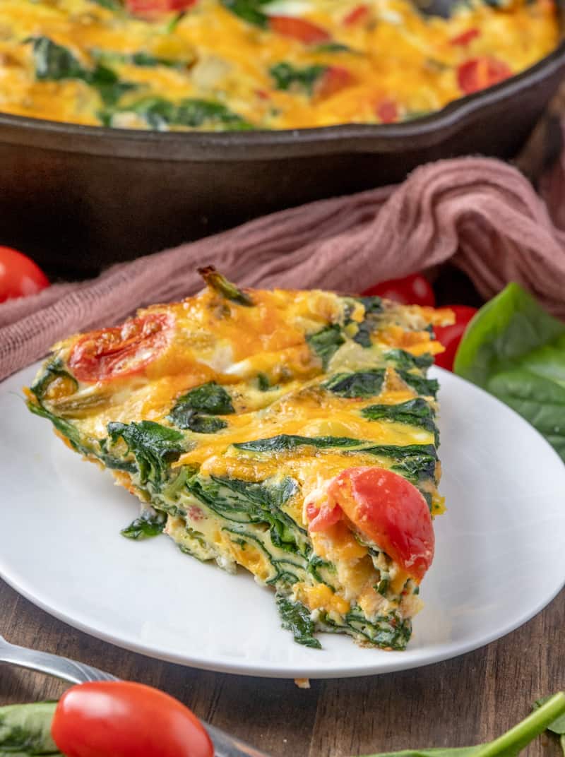 Close up photo of sliced frittata on plate showing spinach and tomatoes 