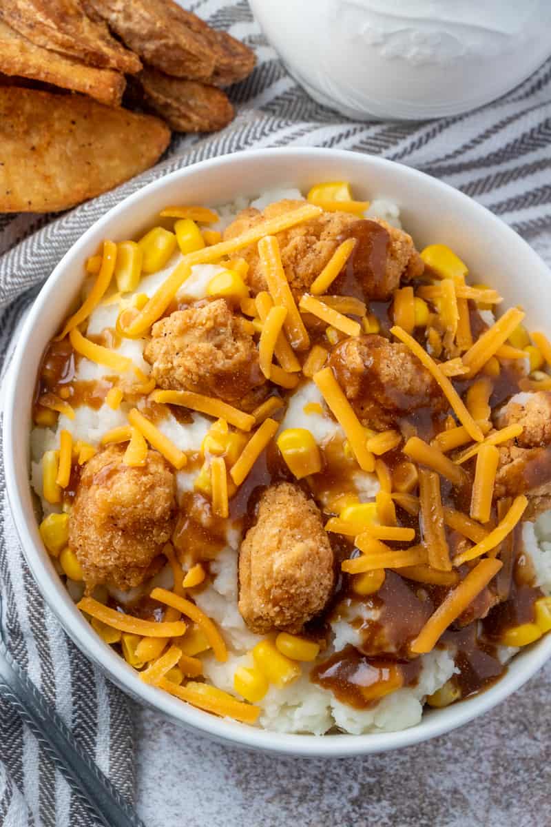 Overhead photo of bowl with potatoes, chicken, corn, gravy and cheese with potato wedges