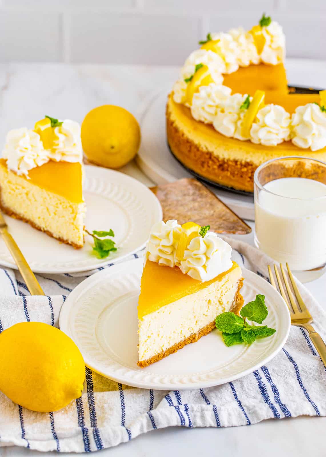 Two slices of cheesecake on white plates garnished with lemon and milk in background.