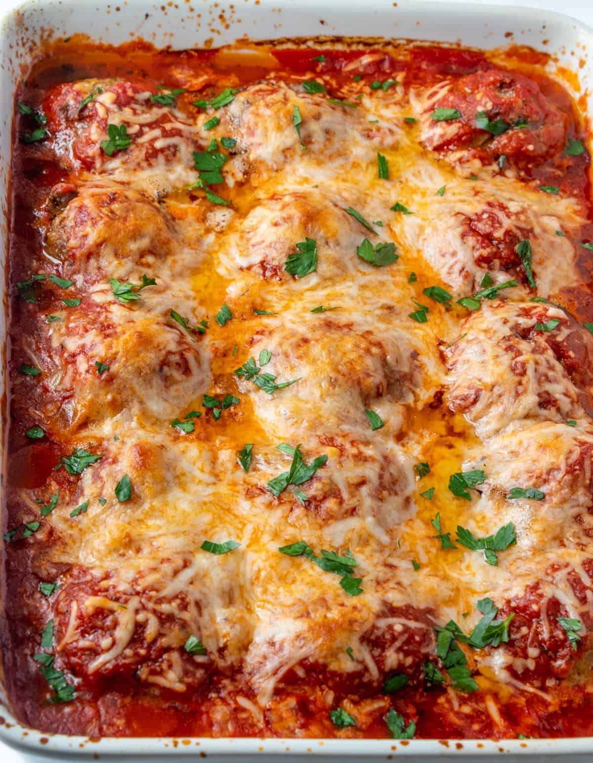 Meatballs in baking dish with melted cheese and sauce topped with parsley