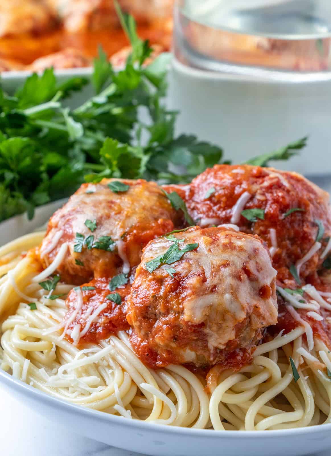 Side photo of meatballs on top of spaghetti with shredded cheese and parsley