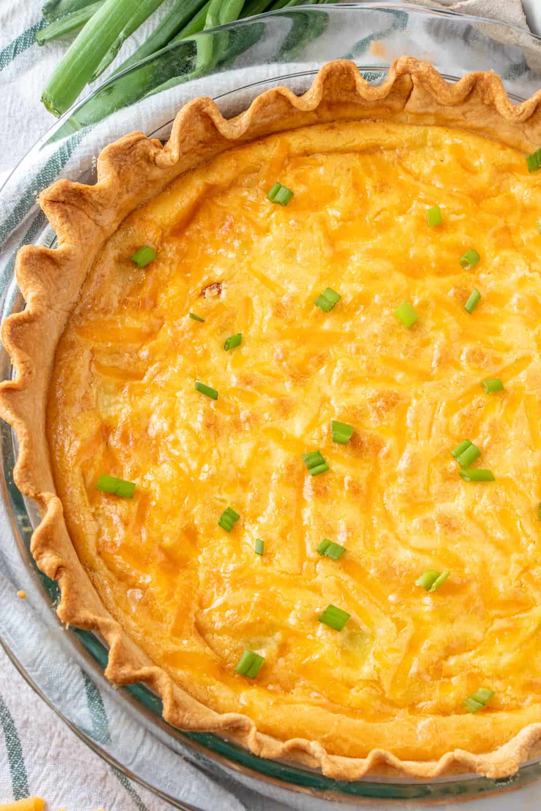 Overhead photo of quiche in pie dish with baked cheese and green onions