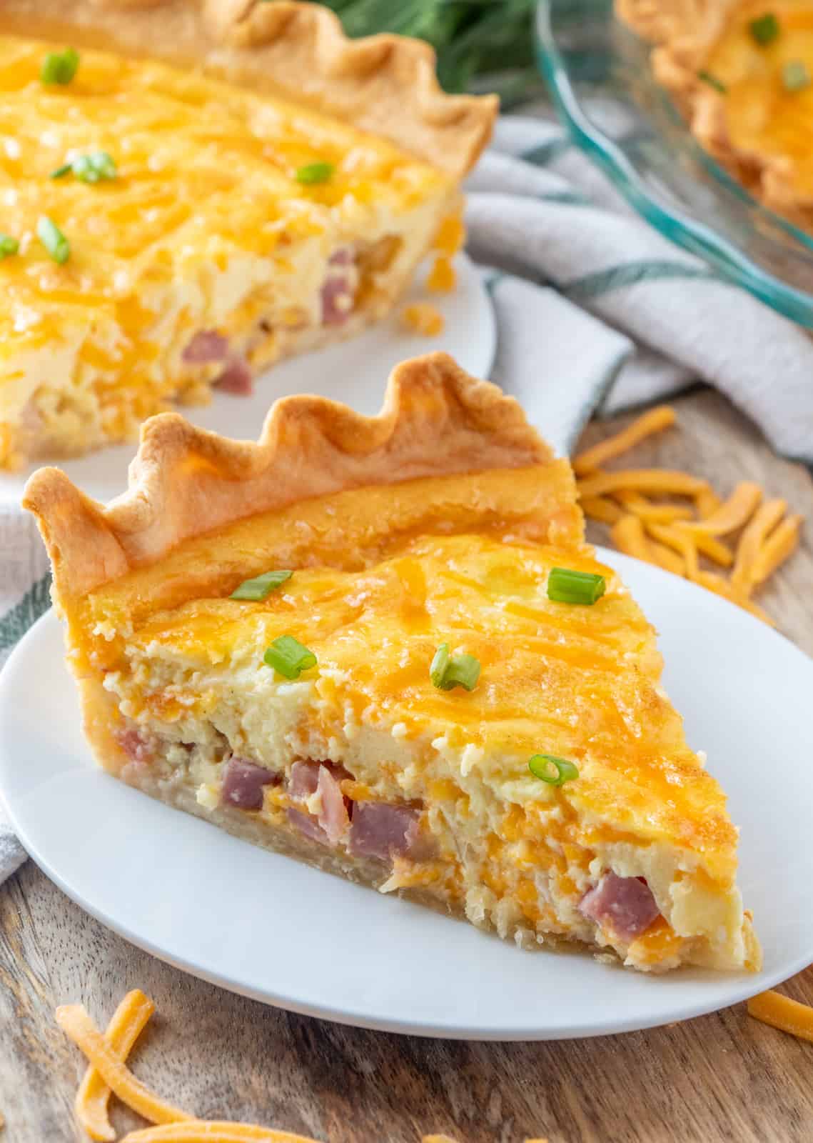 Slice of baked quiche on white plate topped with green onions